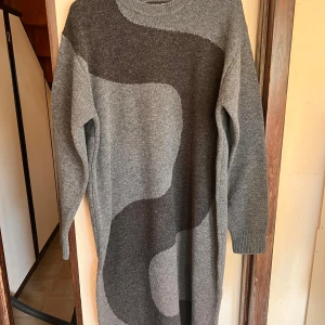 Grå lång stickad klänning från Marimekko x Uniqlo - Säljer en lång, stickad klänning från Marimekko x Uniqlo i olika nyanser av grått med abstrakt mönster. Klänningen har rund halsringning och långa ärmar. Tillverkad i 100% ull för en varm och mysig känsla.