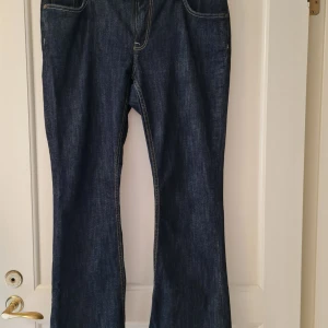 Bootcut jeans från Lindex strl 42 - Mörkblå jeans från Lindex med bootcut-passform och klassiska fickor både fram och bak. Jeansen har kontrastsömmar och är strechiga. Innelängd på benen 75cm. Storlek 42. Kan hämtas i Vallentuna.