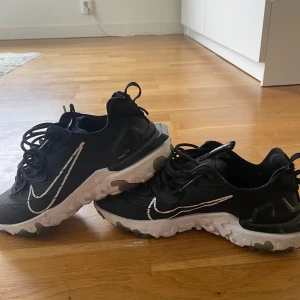 Svarta Nike React sneakers - Säljer ett par svarta Nike React sneakers med vit sula och vit swoosh. Använde kanske 10 gånger och har inga skador eller synliga täcken på användning.