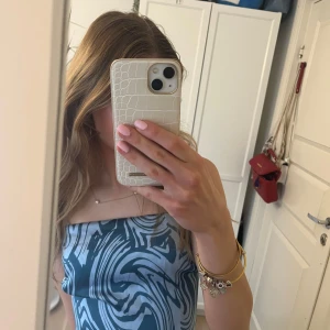 Blå mönstrad linnetopp med rosett - Säljer en snygg linnetopp med blått och grått abstrakt mönster. Toppen har smala axelband, är croppad och har en stor rosett baktill.. Perfekt för sommaren och ger en trendig look. Aldrig använd, endast testad.