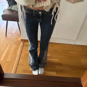 Coola jeans - Säljer ett par mörkblå bootcut jeans med tydliga kontraster längs benen. Klassisk femficksmodell och normal passform. Jeansen har låg midja och stängs med knapp och dragkedja framtill.