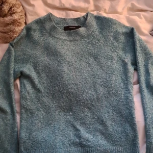 Ljusblå stickad tröja från Vero Moda - Mysig ljusblå stickad tröja från Vero Moda med rund halsringning och långa ärmar. Tröjan har en enkel och klassisk design med ribbade muddar vid ärmslut och nederkant. Perfekt för lager-på-lager under kyliga dagar.