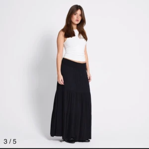 Svart långkjol med volang pris kan diskuteras - Svart långkjol med bred resår i midjan och volangdetaljer. Kjolen har en luftig och flowy passform som ger en avslappnad känsla. Perfekt att styla med en enkel topp eller stickad tröja.