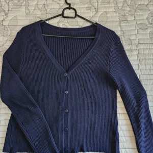 Mörkblå ribbad kofta - Säljer en mörkblå ribbad kofta med v-ringning och långa ärmar. Koftan har knappar framtill och . Perfekt att slänga över en topp eller klänning. Jätte skönt material! Använd 1 gång bara! 