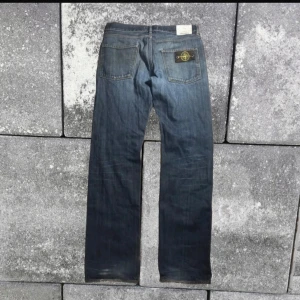 Blå jeansbyxor från Stone Island - Säljer ett par klassiska blå jeansbyxor från Stone Island med rak passform och ikonisk logotyp-patch på bakfickan. Byxorna har fem fickor, knappgylf och en liten skavank där bak vid fickan (se bild 4). Mått- längd 108cm,  Det midja 44cm, lår 30cm, ben 21 cm.