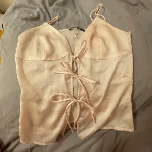 Ljusrosa croppad linnetopp från Gina Tricot - Säljer en ljusrosa croppad linnetopp från Gina Tricot med smala axelband och snygga knytningar framtill. Toppen har en lätt v-ringning och är perfekt för varma dagar.