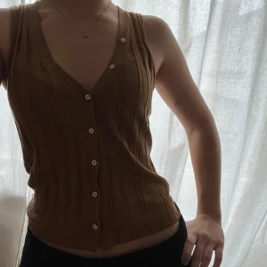 Ribbad linnetopp - Säljer en brun ribbad linnetopp från Lindex med v-ringning och knappar framtill. Toppen är ärmlös och har en croppad passform. Snygg och enkel att matcha med olika outfits.🤎❣️