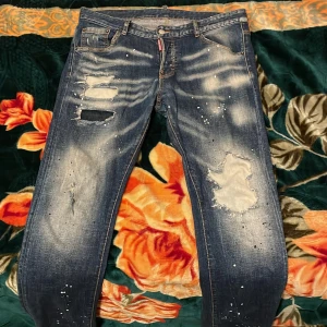 Blå distressed jeans från Dsquared2 - Säljer ett par blå jeans från Dsquared2 med slitningar, hål och färgstänk för en riktigt edgy look. Fick den från min kusin har kvitto till den men inte påse, äkta dsquared2 byxor sitter sköna och bra, vill få bort dem eftersom den är för stor för mig.
