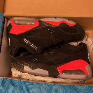 Svarta och röda sneakers från Jordan - Säljer ett par svarta sneakers från Jordan med röda och grå detaljer. Skorna har snörning, rund tå och platt sula. Perfekta för dig som gillar sportig stil och vill sticka ut med snygga färgkontraster.