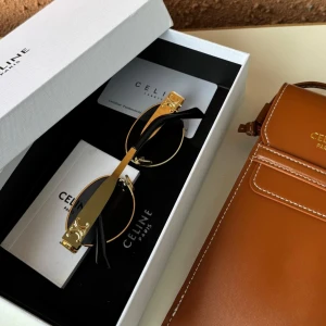 Svarta solglasögon från Celine med guldiga detaljer - Snygga solglasögon från Celine med svarta ovala glas och tunna guldiga metallbågar. Sidorna har Celines ikoniska logga i guld. Perfekt accessoar för en trendig look.