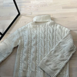 Vit stickad polotröja från BikBok - Säljer en mysig vit stickad polotröja från BikBok med klassiskt kabelstickat mönster. Tröjan har lång och vid ärm och hög polokrage, perfekt för kyliga dagar. Superfin att styla till jeans eller kjol!