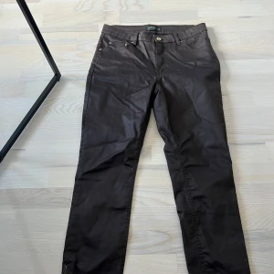 Bruna byxor från STOCKH LM - Snygga läderaktiga bruna byxor från STOCKH LM med klassisk femficksdesign och raka ben. Byxorna har gylf med dragkedja och knapp samt hällor för bälte. Perfekta för en stilren look.