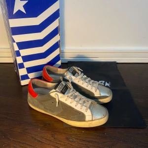 GGDB Superstar sneakers med silver och röd detalj - Säljer ett par GGDB Superstar sneakers med silverfärgad tå, grå sidor och röd häl. Skorna har snörning och en klassisk rund tå. Box och dustbag tillkommer👌Perfekta för dig som gillar en sportig och trendig look. Dm för mer frågor!