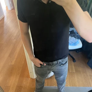 Svart pikétröja från Lacoste - Säljer en klassisk svart pikétröja från Lacoste med krage och knappar framtill. Tröjan har korta ärmar och den ikoniska krokodilloggan broderad på bröstet. Perfekt för en stilren och avslappnad look. Tröjan är i väldigt fint skick och sitter väldigt bra som M. Hör gärna av er om ni har några frågor🙌🙌