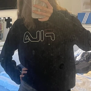 Svart tjocktröjafrån FILA - Svart tjocktröja från FILA med stor logga framtill och mindre logga i nacken. Klassisk rund halsringning och ribbade muddar vid ärmslut och nederkant. Använd ett fårtal gånger. Priset kan alltid diskuteras😊💕