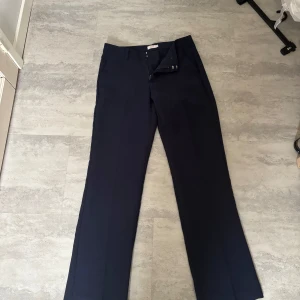 Mörkblå kostymbyxor med raka ben - Snygga mörkblå kostymbyxor med klassisk rak passform och pressveck. Byxorna har hällor för bälte och stängs med dragkedja och knapp. Perfekta för en clean och stilren look.