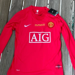 Manchester United 2007/08 Ronaldo #7 - Säljer en röd långärmad Manchester United-tröja från Nike med Ronaldo 7 på ryggen och Champions League-märke på ärmen. Tröjan har AIG som sponsor och detaljer i vitt. Perfekt för fans av klubben och Ronaldo.