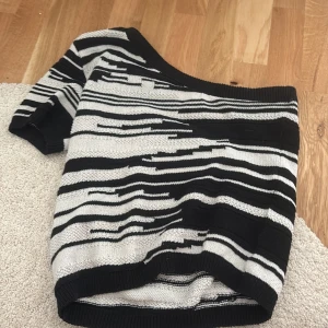 Svartvit stickad tröja från Lindex - Säljer en svartvit stickad tröja från Lindex med unikt randigt mönster. Tröjan har lång ärm och bred ribbad kant vid hals, ärmslut och nederkant. Perfekt för dig som gillar grafiska mönster och vill ha en snygg statement-tröja.