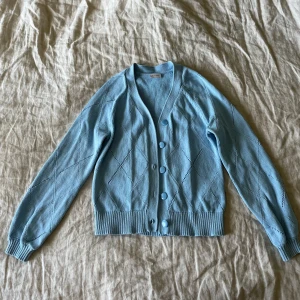 Ljusblå kofta från VILA - Säljer en ljusblå kofta från VILA med v-ringning och knappar framtill. Koftan har ett fint hålmönster, ribbade muddar och är tillverkad i ett stickat material. Upplevs som en något mindre S i modellen, så passar XS-S.