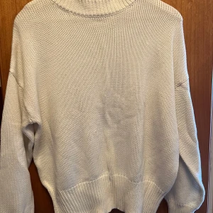 Vit stickad tröja från Lager 157 - Säljer en vit stickad tröja från lager 157 med hög krage och långa ärmar. Tröjan har en avslappnad passform och breda ribbade muddar vid ärmslut och nederkant. Perfekt för kyliga dagar!