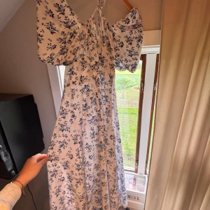 Vit långklänning med blå blommor - Superfin långklänning i vitt med blått blommönster och puffiga korta ärmar. Klänningen har omlottkänsla upptill med knytning vid överdelen av kroppen, bara att skriva om ni vill ha bild på hur den sitter på💗