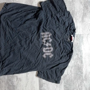 Svart AC/DC t-shirt i bomull - Cool svart t-shirt med klassiskt AC/DC-tryck på bröstet. Skön passform och tillverkad i mjuk bomull, perfekt för dig som gillar rock och vill ha en avslappnad stil. Rund halsringning och korta ärmar.