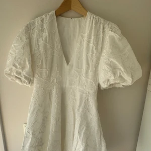 Vit kortklänning med puffärm och broderade blommor - Superfin vit kortklänning med puffiga ärmar och v-ringning. Klänningen har broderade blommor över hela tyget och en lätt ballongformad nederkant. Perfekt för sommaren eller student! ❤️ kan mötas upp