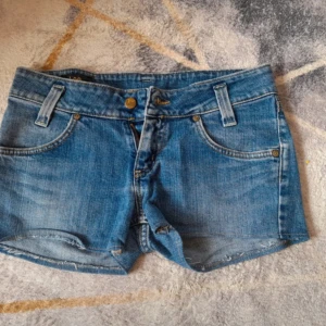 Blå jeansshorts från Lee - Snygga blå jeansshorts från Lee i storlek XS med klassisk femficksdesign. Modellen är lågmidjad och har råa kanter nertill för en avslappnad vibe. Perfekta för varma dagar och enkel att matcha med allt. Skulle säga att den passar som både XS och S.