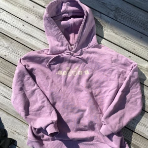 Ljuslila hoodie från Pull&Bear - Säljer en ljuslila hoodie från Pull&Bear med tryck framtill och en stor fjäril på ryggen. Tröjan har huva med dragsko och ribbade muddar. Perfekt för dig som gillar färg och snygga detaljer!