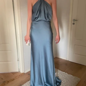 Blå långklänning från ASOS Edition - Snygg blå långklänning från ASOS Edition i glansigt material med halterneck och öppen rygg. Klänningen har en elegant draperad överdel och figurnära passform som faller snyggt mot golvet. Perfekt för bal eller festkväll! Jag säljer nu en balklänning från asos som inte är använd. Det är storlek 34.☺️ Obs: Alla knappar är inte knäppta i nacken på bilderna. Därför klänningen blir lite hängig.