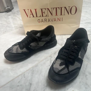 Valentino rockrunners ( kvitto finns)  - Snygga Valentino Garavani Rockrunner sneakers i svart och grått med coolt kamouflagemönster. Skorna har detaljer i mocka och skinn, samt nitar på hälen för en edgy vibe. Klassisk snörning och rund tå. Perfekta för dig som vill sticka ut med lyxig streetstyle.