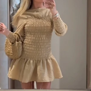Beige kort klänning med volang - Supersöt beige kort klänning med smockad överdel och långa ärmar. Klänningen har en volangig kjol och är i storlek S. 