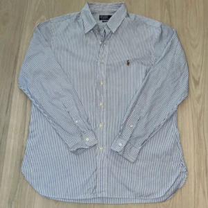 skjorta Polo Ralph Lauren - Klassisk blå- och vitrandig skjorta från Polo Ralph Lauren i bomull. Custom fit-modell med lång ärm, knappar framtill och broderad logga på bröstet. Perfekt för en clean och stilren look. Skriv för mer information🙌