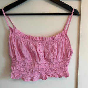 Söt rosa linnetopp - Rosa croppad linnetopp från Stradivarius med smala justerbara axelband och volangkant nertill. Toppen har rynkad struktur och är perfekt nu inför sommaren💕 Aldrig använd men har tyvärr klippt av lapparna. Storlek S.
