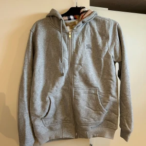 Grå hoodie med dragkedja från Burberry - Säljer en Grå burberry hoodie i storlek M. Kan även passa S då den blivit lite mindre i tvätten