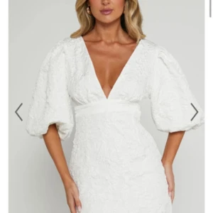 Vit studentklänning Showpo - Supersnygg vit studentklänning från showpo med djup v-ringning och stora puffärmar. Klänningen har en figurnära passform upptill och markerad midja. Materialet är strukturerat och ger en lyxig känsla. Perfekt för speciella tillfällen! Storlek 38, ny med prislapp!❤️Modellen heter Miley mini dress