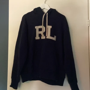 POLO Ralph lauren hoodie - Snygg mörkblå hoodie från Polo Ralph Lauren med stora vita RL-bokstäver på bröstet. Klassisk huva med snörning och långa ärmar. Perfekt för dig som gillar en stilren och sportig look. Nypris 5000kr säljer för 1800