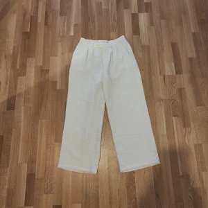 Vita vida byxor i linne, glitterdetaljer - Snygga och luftiga vita byxor med medium midja och vida ben. Perfekta för varma dagar och har en klassisk look med diskreta veck framtill. Stängs med dragkedja och knapp i midjan.