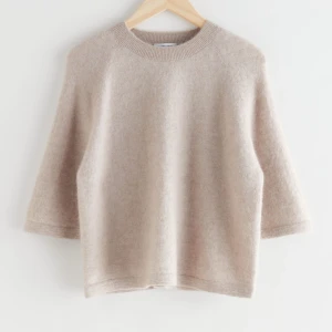 Beige stickad tröja från & Other Stories - Mysig beige stickad tröja från & Other Stories med rund halsringning och trekvartsärm. Tröjan har en enkel och stilren design, perfekt för lager-på-lager och passar till många olika outfits.