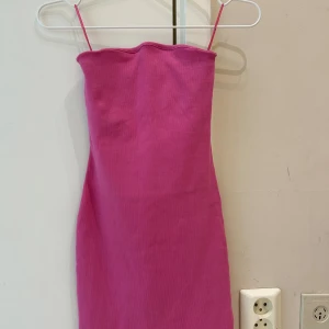 Rosa ribbad kortklänning  - Säljer en rosa ribbad kortklänning har en enkel och stilren design med rak halsringning och figurnära passform. Perfekt för dig som gillar färg och vill sticka ut.