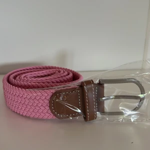 Ljusrosa flätat bälte  - Säljer ett rosa flätat bälte med silverfärgat metallspänne och bruna skinn-detaljer vid spännet. Bältet har en snygg och ungdomlig look, perfekt för att ge outfiten lite extra färg.