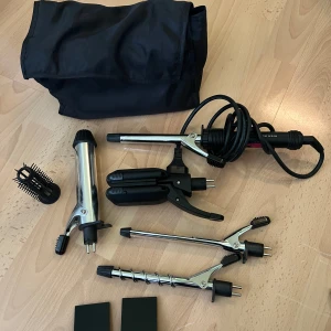 Multistyler för hår med flera tillbehör - Säljer en multistyler för hår med flera utbytbara tillbehör, inklusive locktänger i olika storlekar, borste och plattång. Allt i svart och silver metall och plast, med tillhörande svart förvaringsväska. 