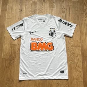 Vit Santos FC fotbollströja från Nike - Säljer en vit Santos FC fotbollströja (remake) från Nike med tryckta sponsorer som BMG och Netshoes. Tröjan har klubbmärke på bröstet, svart Nike-logga och är tillverkad i Dri-FIT-material för bra ventilation. Klassisk passform och korta ärmar. Helt ny endast testad! Perfekt tröja inför sommarn om du frågar mig☺️