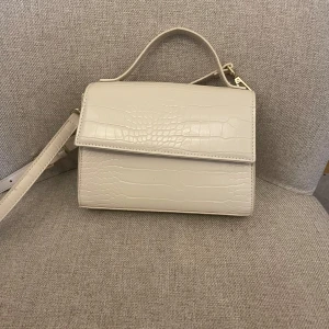 Vit handväska - Snygg vit axelväska med croco-mönstrad yta och stilren design. Väskan har både handtag och justerbar axelrem, samt ett praktiskt innerfack med dragkedja. Endast använt en gång så bra skick!               20x16cm.                                                                     Nypris 399