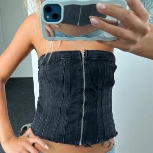 Svart jeanskorsett med dragkedja - Svart axelbandslös korsett i jeansmaterial med silverfärgad kedja. Använd 1 gång 