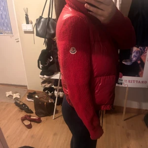 Röd pufferjacka från Moncler - Säljer en röd pufferjacka från Moncler med stickade ärmar och hög krage. Jackan har dragkedja framtill och två fickor med dragkedja. Knappt använd