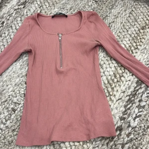 Rosa ribbad topp med dragkedja  - Supersnygg rosa ribbad topp från New Yorker med lång ärm och en dragkedja framtill. Stretchigt material. Storlek S