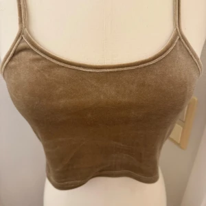 Beige topp i sammetsmaterial XS - Säljer en beige gullig kort topp med smala axelband och mjuk sammetskänsla. XS.  Aldrig använd. Toppen har en enkel och stilren design som passar perfekt till jeans eller kjol. Häntas i Hägersten eller skickas. 