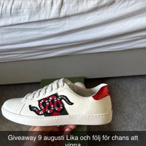 Gucci sneakers med orm brodyr - Snygga vita sneakers från Gucci med ikonisk röd och svart orm brodyr på sidan och röd metallic-detalj på hälen. Skorna har klassisk snörning och är tillverkade i skinn. Perfekta för dig som vill sticka ut med en lyxig och trendig look.