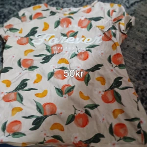 Beige t-shirt med fruktmönster - Snygg beige t-shirt med färgglatt fruktmönster i orange, gul och grönt. Trycket på bröstet säger 'Forever'. Perfekt för dig som gillar lekfulla och somriga vibes. Kortärmad och i mjukt bomullstyg.